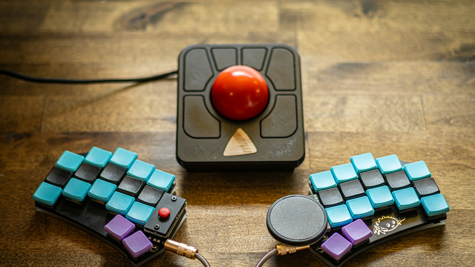 A split keyboard in two halves with a trackball between them on a wooden desk