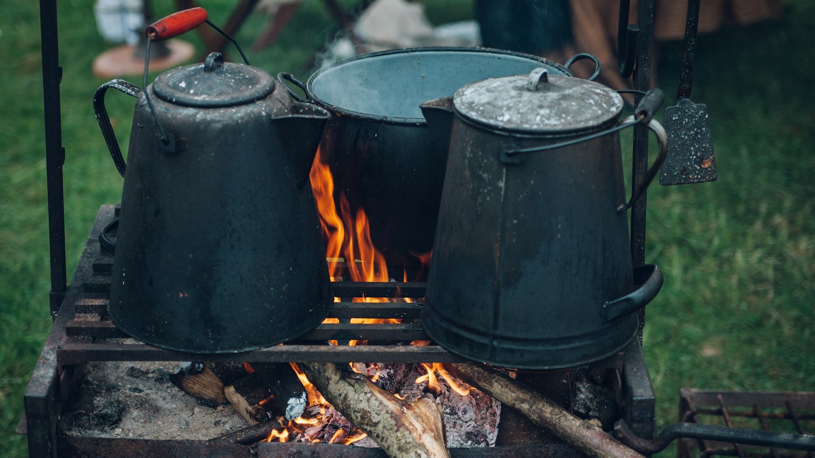 Two coffee kettles and a pot heating over a campfire