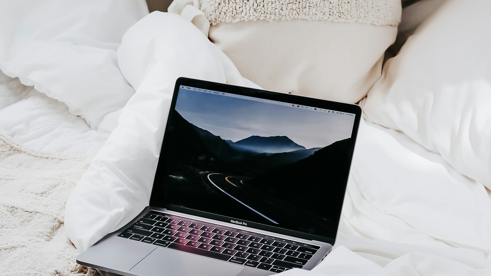 An open laptop resting on a white duvet and pillows