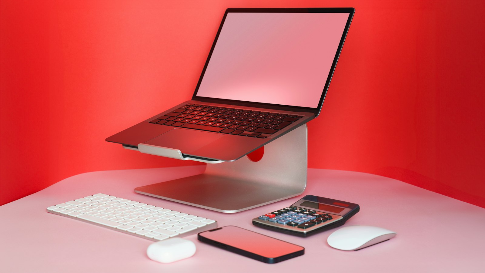 A laptop raised on a silver aluminum stand next to a white keyboard and mouse