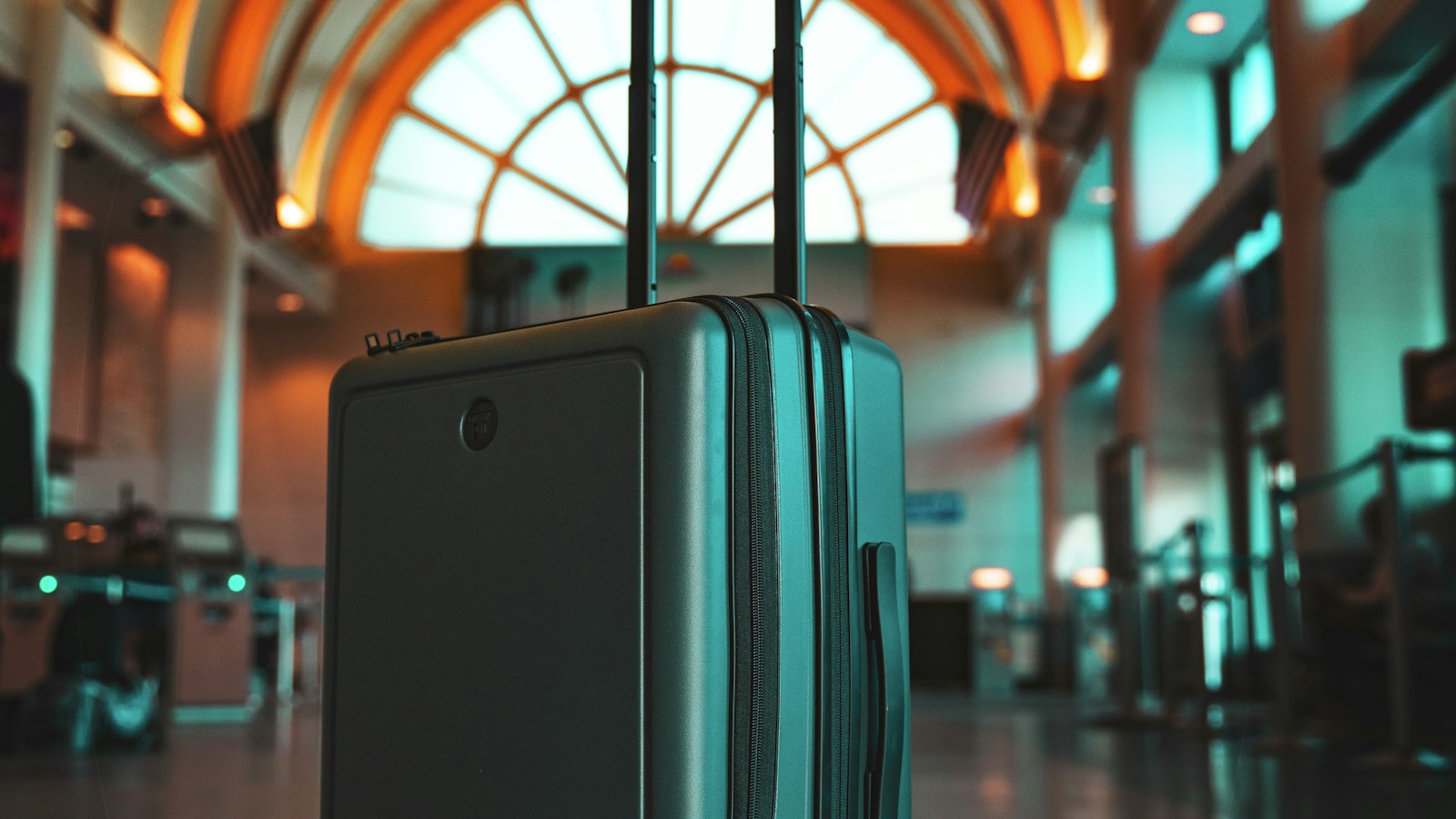 A gray hard-shell suitcase with its handle raised in an airport terminal