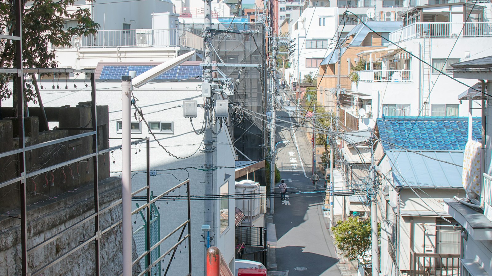 A narrow Tokyo street with overhead power lines, seen from a stairway